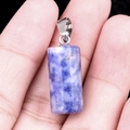 Blue and white natural crystal cylinder pendant with silver clasp held by hand - Sodalite