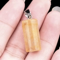 Translucent yellow crystal cylindrical pendant with silver bail shown in hand - Yellow Jade