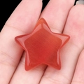 Piedra de estrella de opalo rojo con efecto ojo de gato sostenida en la mano - Rojo
