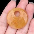 Pendente in pietra arancione traslucida tenuto in mano con finitura lucida - Giada Gialla