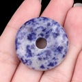 Pendentif donut en sodalite bleu et blanc poli tenu en main pour création bijoux - Jaspe à Points Bleus