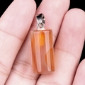 Orange carnelian crystal cylinder pendant with silver bail shown in hand for scale - Red Agate