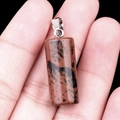 Hand holding a 20mm mahogany obsidian cylindrical pendant with silver metal bail - Mahogany Obsidian