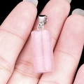 Polished natural rose quartz cylinder pendant with silver bail shown in hand - Rose Quartz
