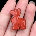 Polished red jasper carved deer gemstone figurine held in hand on black background - Red Jasper