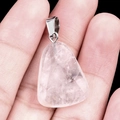 Trapeze shaped rose quartz crystal pendant with polished silver clasp held in hand - White Crystal