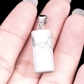 Hand holding white turquoise cylinder stone pendant with silver clasp on black background - Howlite