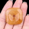 Ciondolo quadrato in quarzo arancione lucido tenuto in mano con vista traslucida - Giada Gialla