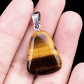 Polished trapezoid tiger eye stone pendant with yellow brown stripes held in hand - Tiger's Eye