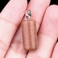 Polished Goldstone cylinder pendant in reddish brown with silver clasp on a hand - Gold Sand Stone (Synthetic)