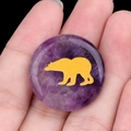 Polished natural purple amethyst stone disc with gold bear engraving held in hand - Amethyst