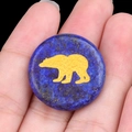 Lapis lazuli stone disc with gold polar bear engraving held between fingers - Lapis Lazuli
