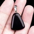 Polished black trapezoid gemstone pendant with silver metal bail held in hand - Obsidian
