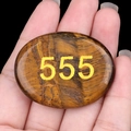 Tiger Eye palm stone featuring engraved gold number 555 held in a hand for size comparison - Tiger's Eye