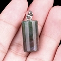 Green and purple natural crystal cylinder pendant with silver bail shown in hand - India Agate