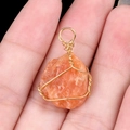 Handmade orange raw gemstone pendant wrapped in gold wire held in hand for scale - Sunstone