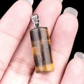Handheld view of a tiger eye stone cylinder pendant with a silver metal clasp - Tiger's Eye