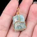 Amazonite gemstone pendant with gold wire wrap held by hand against black background - Amazonite