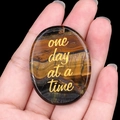 Pierre œil de tigre tenue en main avec phrase motivante dorée One Day At A Time - Œil de tigre