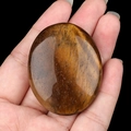 Polished natural tiger eye palm stone in hand showing golden brown chatoyancy - Tiger's Eye