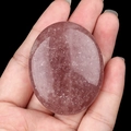 Polished oval pink strawberry quartz palm stone for massage held in hand on black background - Strawberry Quartz