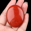 Polished Red Jasper oval palm stone with natural black veins held in a hand - Red Jasper