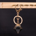 Golden keychain with black resin diamond pendant and crown detail on black background - Obsidian