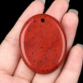 Polished oval red jasper stone pendant with black spots held in hand - Red Jasper