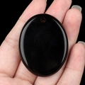 Polished black obsidian oval palm stone pendant being held in hand for size visualization - Obsidian