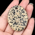 Dalmatian Jasper oval stone pendant held in hand showing natural black spot patterns - Dalmatian Jasper