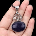 Handheld view of oval blue sandstone pendant with silver filigree and black cord - Blue Sandstone (Artificial)
