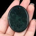 Oval dark green semi-precious stone pendant with pre-drilled hole held in hand - India Agate
