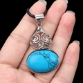 Vintage oval blue stone pendant with silver filigree detail and black cord on hand - Blue Turquoise (Synthetic)