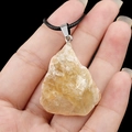 Pendentif en pierre de cristal jaune naturel avec cordon noir tenu à la main sur fond noir - Citrine