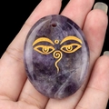 Natural amethyst palm stone pendant with golden Buddha eyes symbol in hand - Amethyst