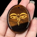Oval tiger eye stone pendant featuring a golden Buddha eye engraving on hand - Tiger's Eye