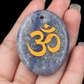 Pendentif ovale en lapis-lazuli avec symbole Om doré tenu dans la main - Aventurine Bleue