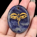 Handheld oval blue lapis lazuli palm stone pendant with golden Buddha eye engraving - Blue Sodalite