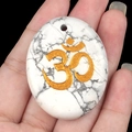 Pierre de paume ovale en turquoise blanche avec symbole Om doré tenu en main - Howlite