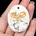 Oval white turquoise pendant with golden Buddhist wisdom eyes and natural gray texture - Howlite