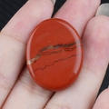 Pietra di diaspore rosso ovale lucidata con venature naturali tenuta in mano - diaspro rosso