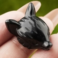 Polished black obsidian fox head carving held in hand with natural green background - Obsidian