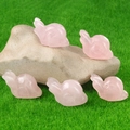 Miniature rose quartz rabbit figurines displayed on natural stone and green moss - Rose Quartz