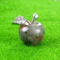 Handcrafted crystal apple ornament with red-brown veins on vibrant green grass - African Blood Stone