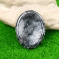 Pietra di labradorite lucidata a forma ovale appoggiata su uno sfondo di erba - Larvikite
