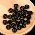 Polished black obsidian rune stone set with golden Norse symbols in a wooden tray - Obsidian