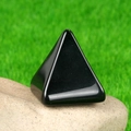 Polished black obsidian pyramid energy stone for home decor displayed on a natural rock - Obsidian