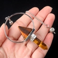 Tiger eye stone crystal pendulum with hexagonal column and silver chain held in hand - Tiger's Eye