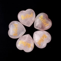 Five heart-shaped pink rose quartz stones with gold Belief engraving on black background - Belief