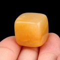 Polished 16mm yellow translucent crystal stone cube held between fingers on black background - Topaz